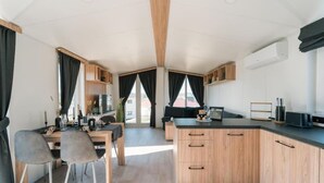 A modern kitchen with wooden cabinets, a dining area with two chairs, and a large window with curtains.