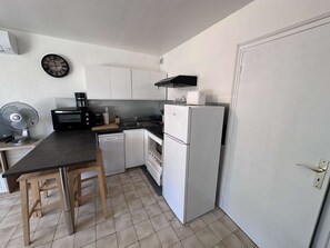 A compact kitchen with white cabinets, a black countertop, a white refrigerator, a coffee maker, and a wall clock.