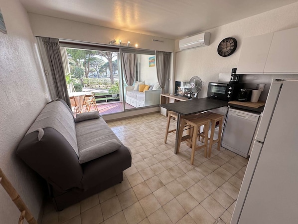 A compact living space with a sofa, a dining table, a kitchen area with a microwave, and a refrigerator.