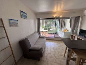 A living area with a sofa, a dining table, and a TV. There is a sliding glass door leading to an outdoor area.