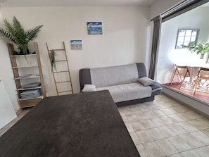 A living room with a grey sofa, a wooden ladder, a plant, and a painting on the wall.