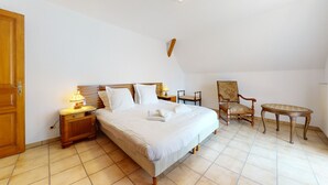 Quarto com cama, cadeira, mesa pequena e mesa de cabeceira com abajur.