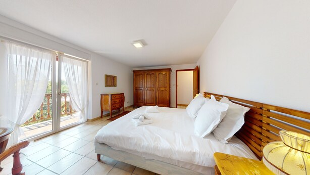 Quarto com cama, guarda-roupa de madeira e uma pequena mesa.