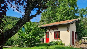 Ein kleines Haus mit roter Tür und Fenstern, umgeben von üppigem Grün und blauem Himmel.