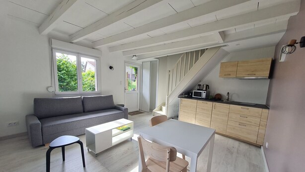 Ein moderner, offener Wohnbereich mit grauem Sofa, weißem Couchtisch, einem Holzesstisch und einer Küchenzeile mit Holdekor und einer Mikrowelle.