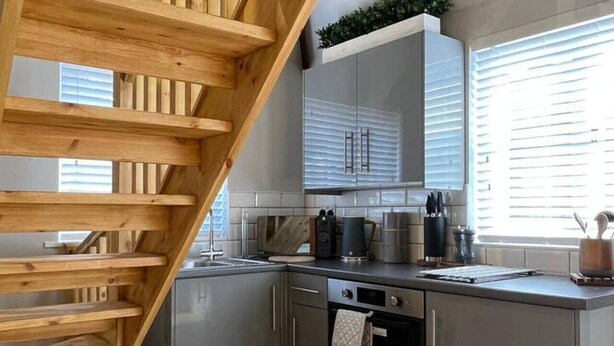 Una cocina moderna con una escalera de madera, armarios grises y una ventana con persianas.