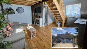 Un interior acogedor con techo de madera, un sofá, una pequeña mesa, una escalera y una zona de cocina.