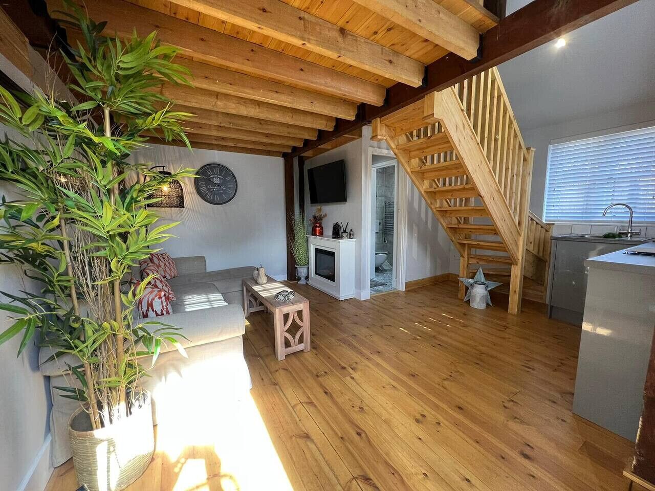 A spacious living area with wooden flooring, a staircase, a sofa, a small table, and a large potted plant.