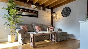 Una sala de estar acogedora con piso de madera, un conjunto de sofá, una mesa de centro, una planta en maceta y un reloj de pared.