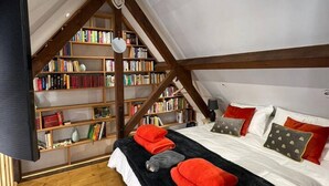 Un dormitorio con techo inclinado, una estantería de madera, una cama con almohadas rojas y grises, y una manta de color negro.