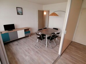 A room with a dining table, chairs, a television on a cabinet, and a door leading to another room.