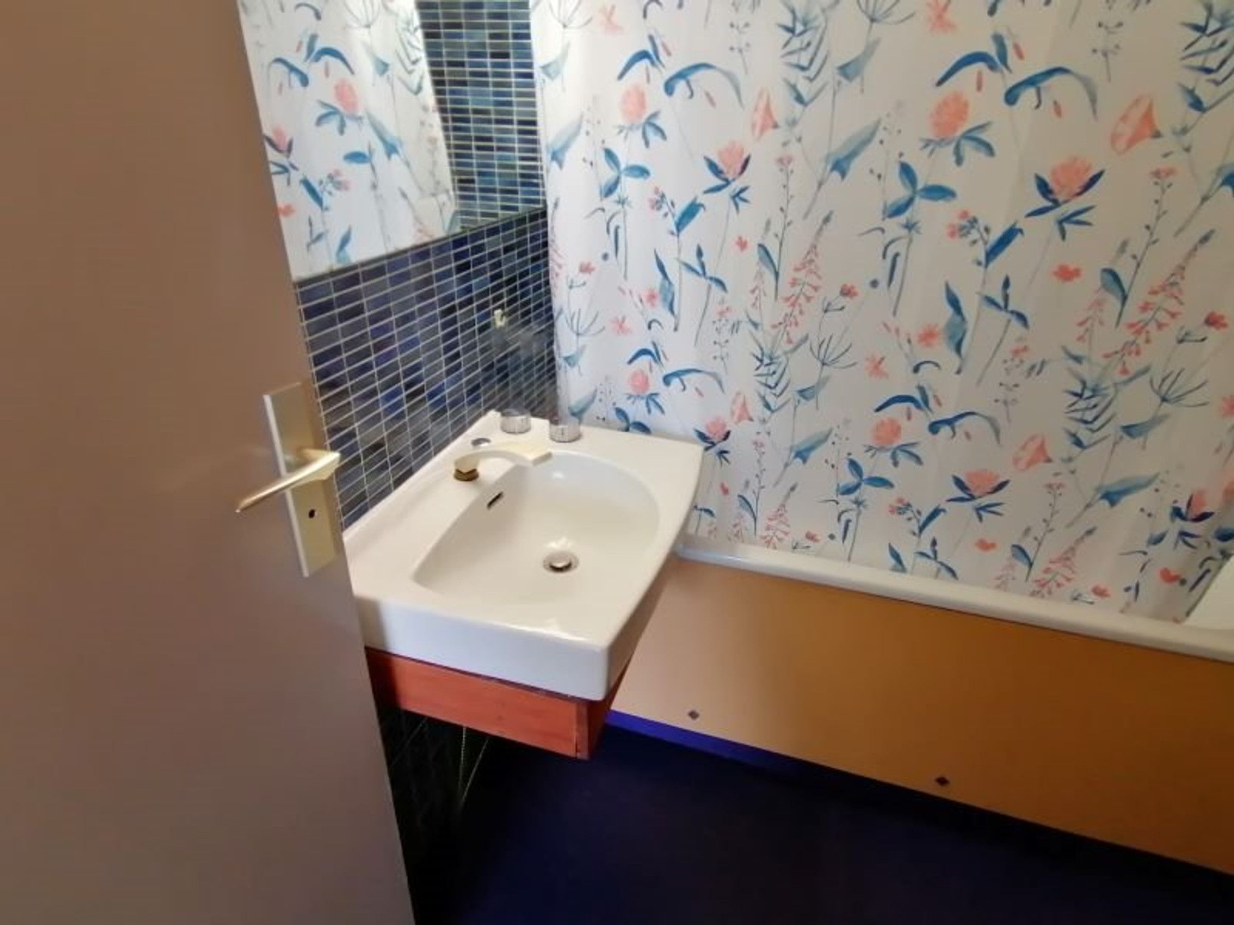 Ett badrum med ett vitt handfat, en spegel och blommig tapet.
