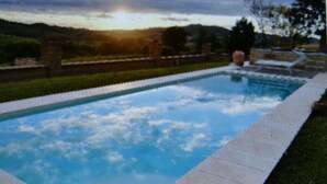 Une piscine rectangulaire dont le bord est recouvert de carreaux, entourée d’une pelouse et d’un petit muret en pierre.