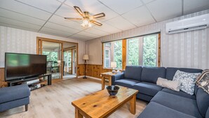 Ein modernes Wohnzimmer mit Flachbildfernseher, Couchtisch aus Holz, blauem Sofa und Deckenventilator.