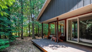 Ein modernes Haus mit einer Holzdachterrasse, großen Fenstern und einem bewaldeten Hintergrund.