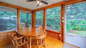 Ein Esszimmer mit Holzboden, einem runden Tisch und Stühlen, großen Fenstern und einem Deckenventilator.