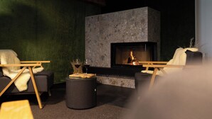 A modern living room with a stone fireplace, two armchairs, and a round ottoman. - Köpfle Alpe (Balderschwang)