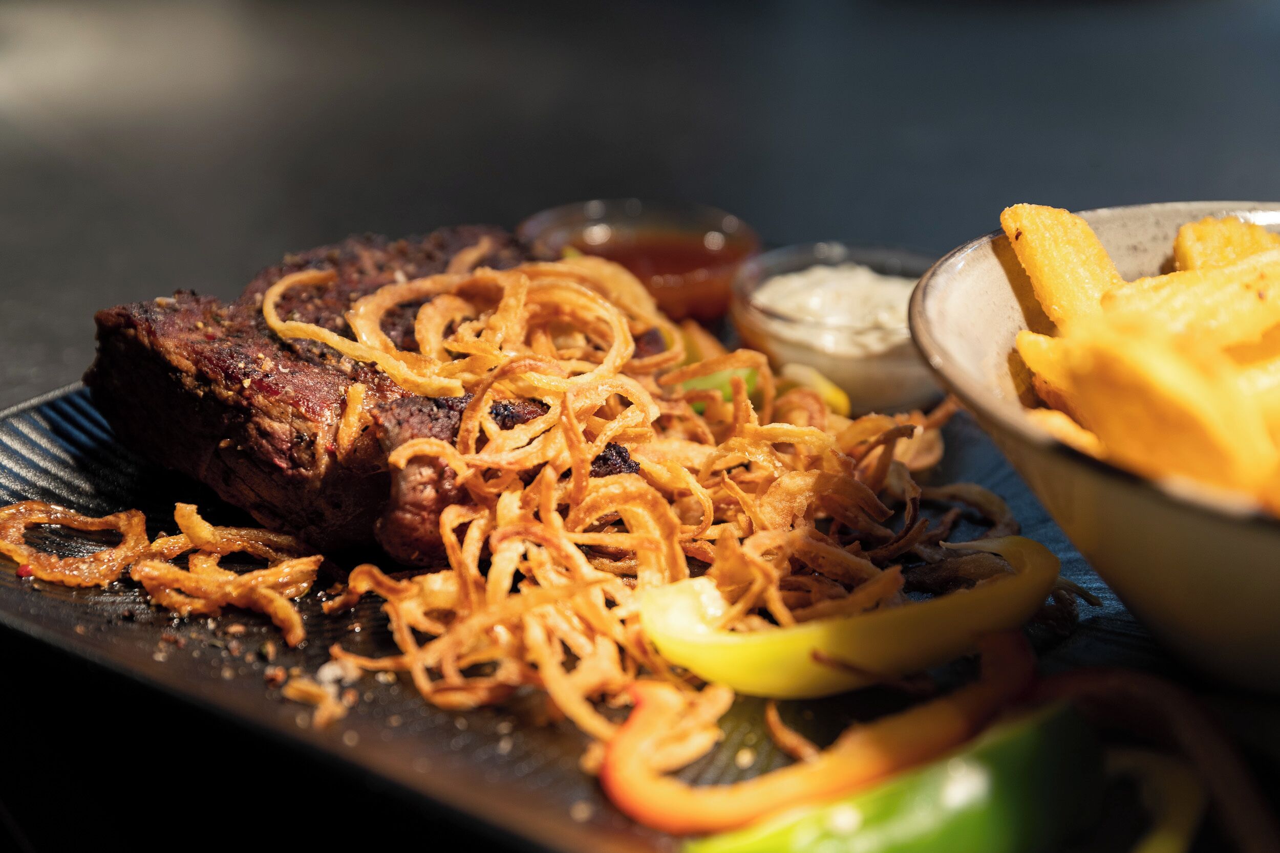 Ein Teller mit gegrilltem Fleisch, karamellisierten Zwiebeln und einer Schüssel Pommes.