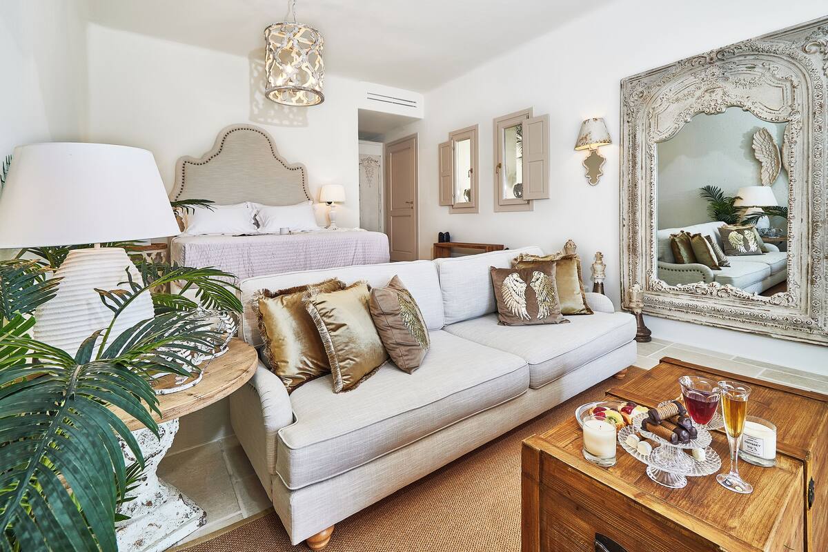 A well-lit room with a bed, a sofa, a coffee table with snacks, and a large mirror.