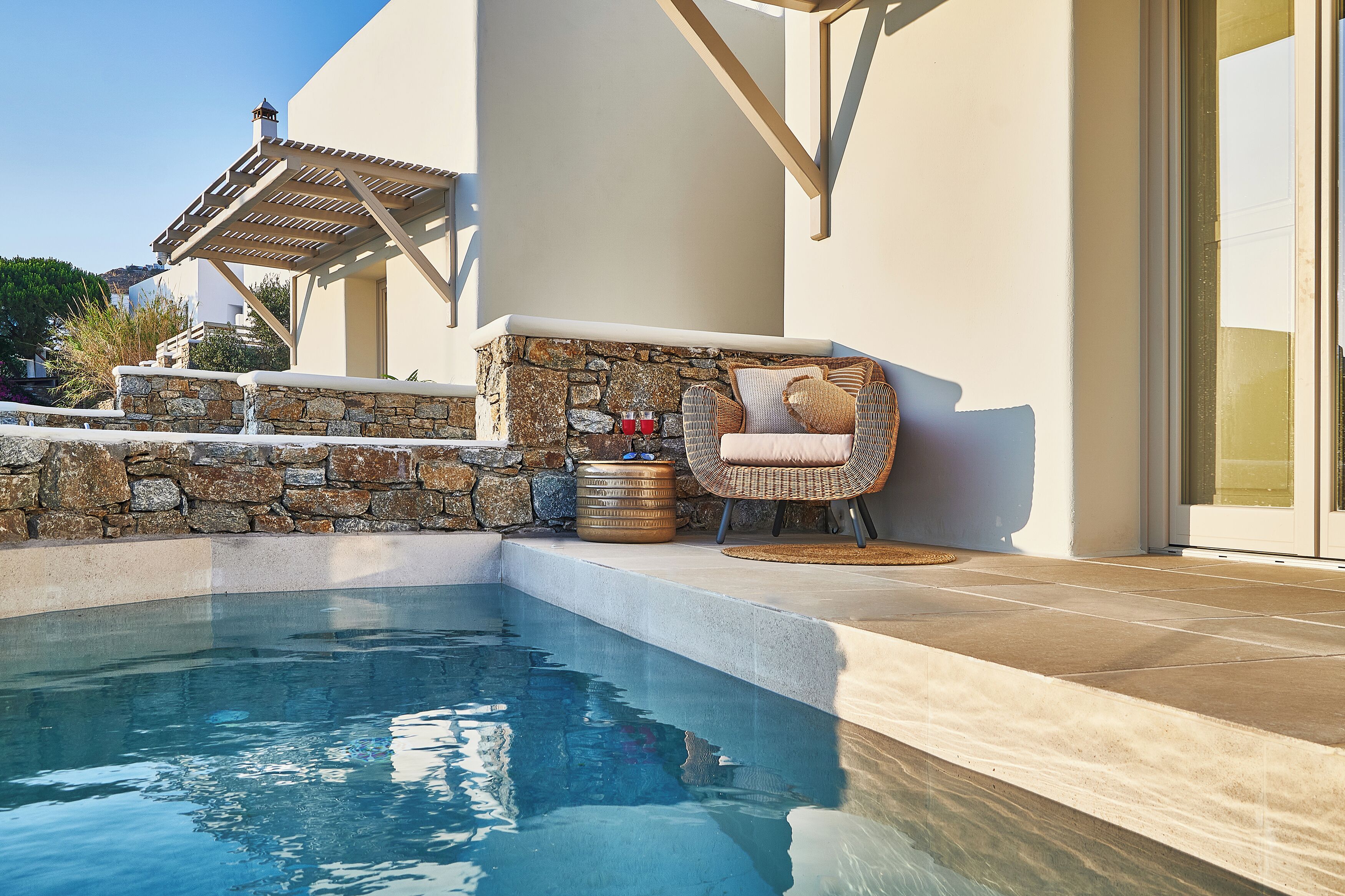 A swimming pool with stone walls and a wicker chair.