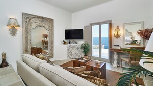 A living room with a sofa, a television, a large mirror, and a view of the sea through a glass door. - Aqua Mykonos Suites - Adults Only (Mykonos)