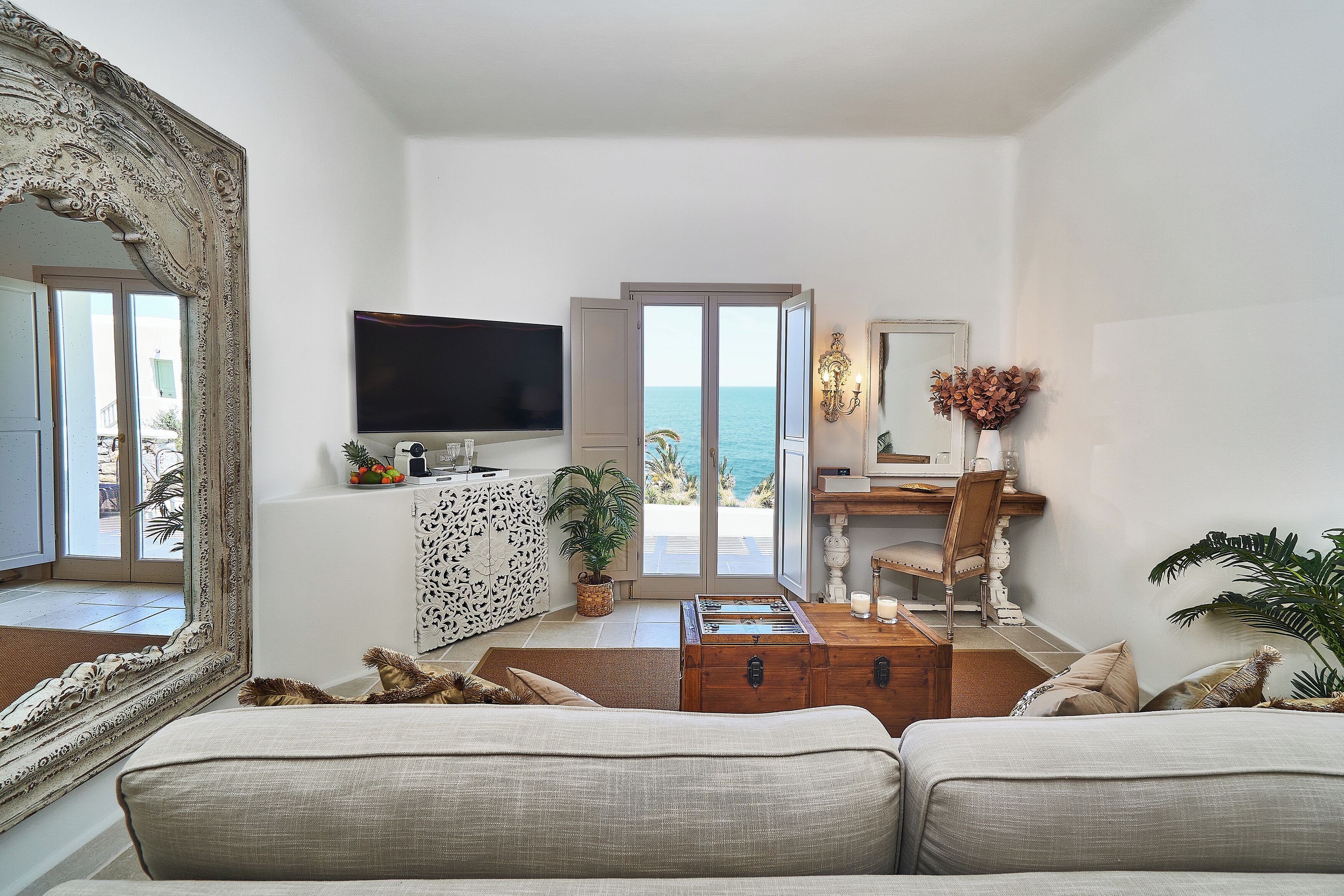 A living room with a large mirror, a television, a foosball table, and a view of the sea through a glass door.