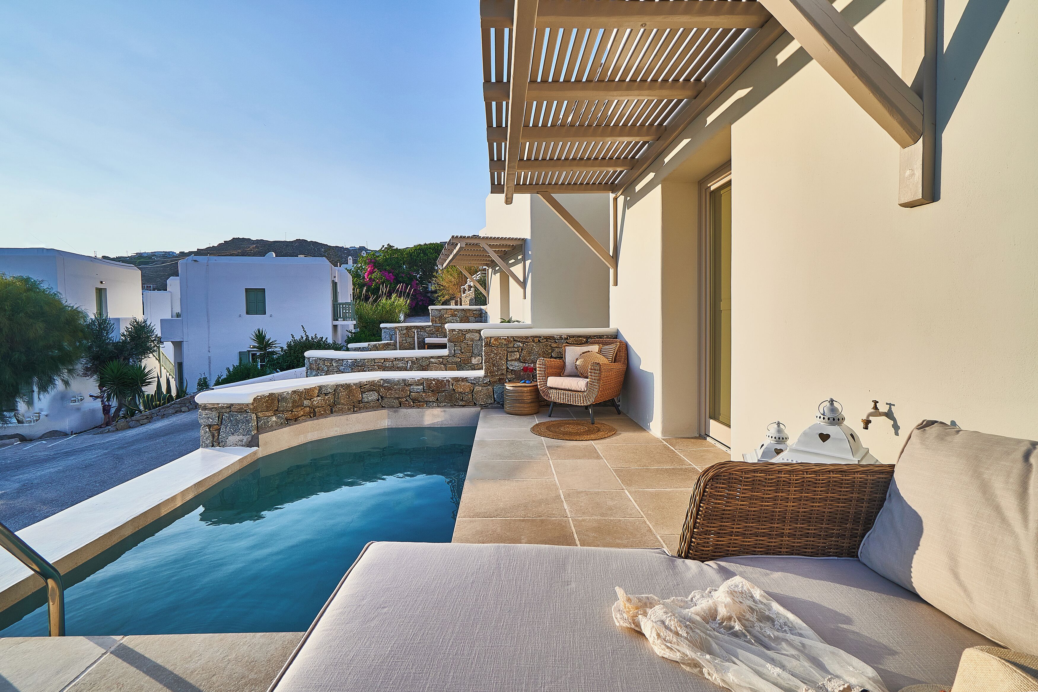 A poolside area with a lounge chair, a wicker chair, and a small table with a lamp.