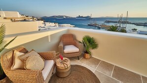 A balcony with wicker furniture, a potted plant, and a view of the sea and ships. - Aqua Mykonos Suites - Adults Only (Mykonos)