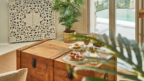 A wooden chest with a latch, a decorative white cabinet, a potted plant, and a table with food and drinks. - Aqua Mykonos Suites - Adults Only (Mykonos)