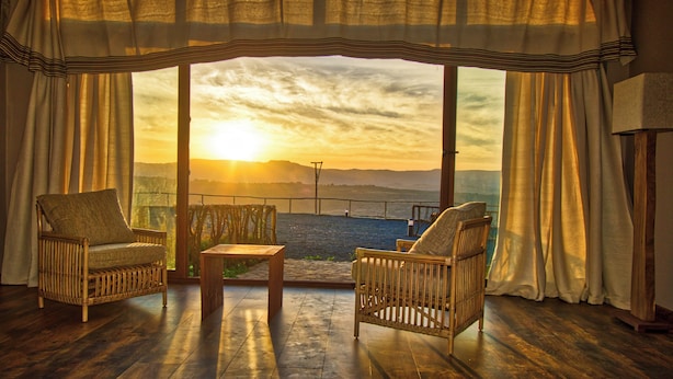 Una habitación con dos sillones de mimbre, una mesita y vistas al atardecer sobre el agua.