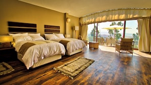 Habitación de hotel con dos camas, un área de descanso con una mesa y sillas, y vistas al exterior.