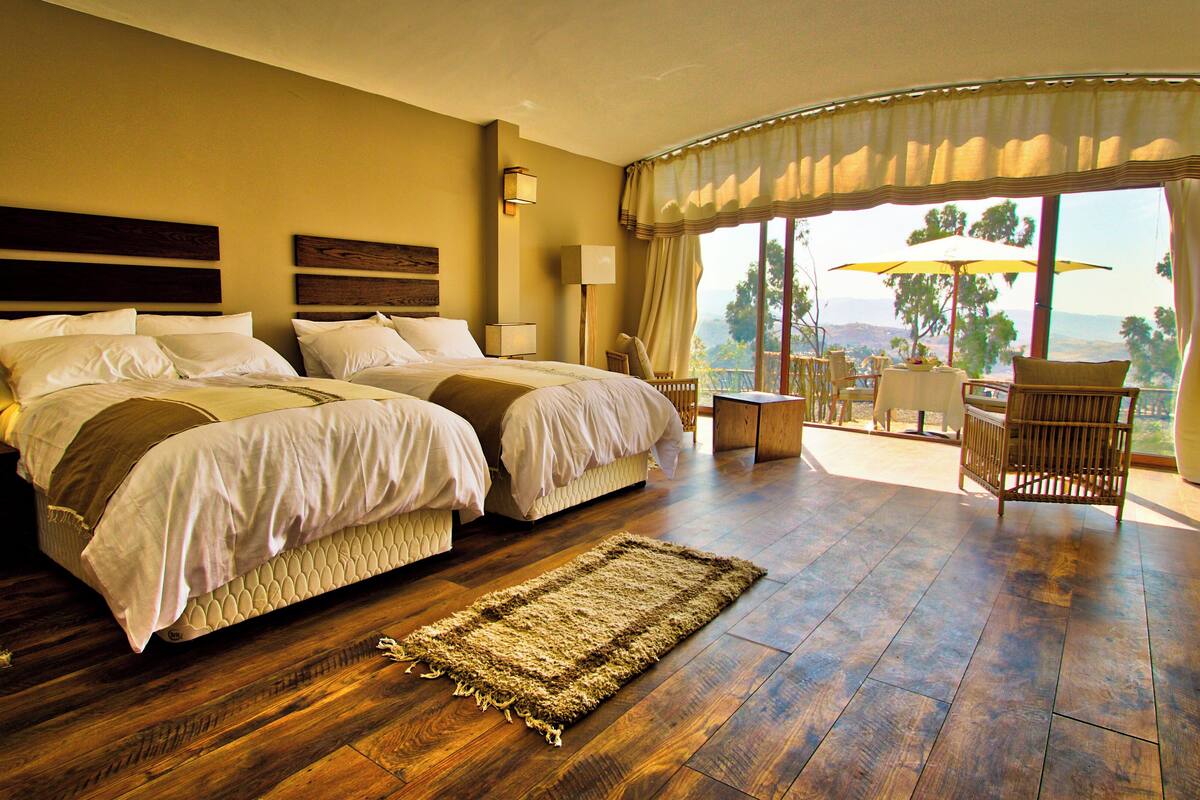 A hotel room with two beds, a sitting area with a table and chairs, and a view of the outdoors.