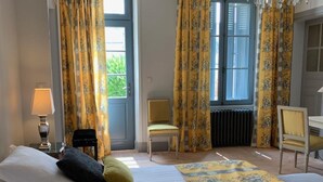 A hotel room with a large bed, two chairs, a desk, and yellow curtains. - Charming cottage with garden near castles, WiFi, parking included (Benais)