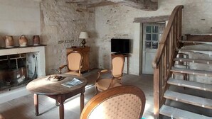 A rustic room with exposed wooden beams, a fireplace, a television, and a staircase. - Charming cottage with garden near castles, WiFi, parking included (Benais)