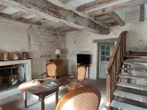 Une pièce rustique avec des poutres apparentes, une cheminée, un téléviseur et un escalier.