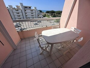 A balcony with a table and chairs, a tiled floor, and a view of buildings and trees. - 2-room apartment with terrace and parking in Le Grau-du-Roi for 4 people (Le Grau-du-Roi)