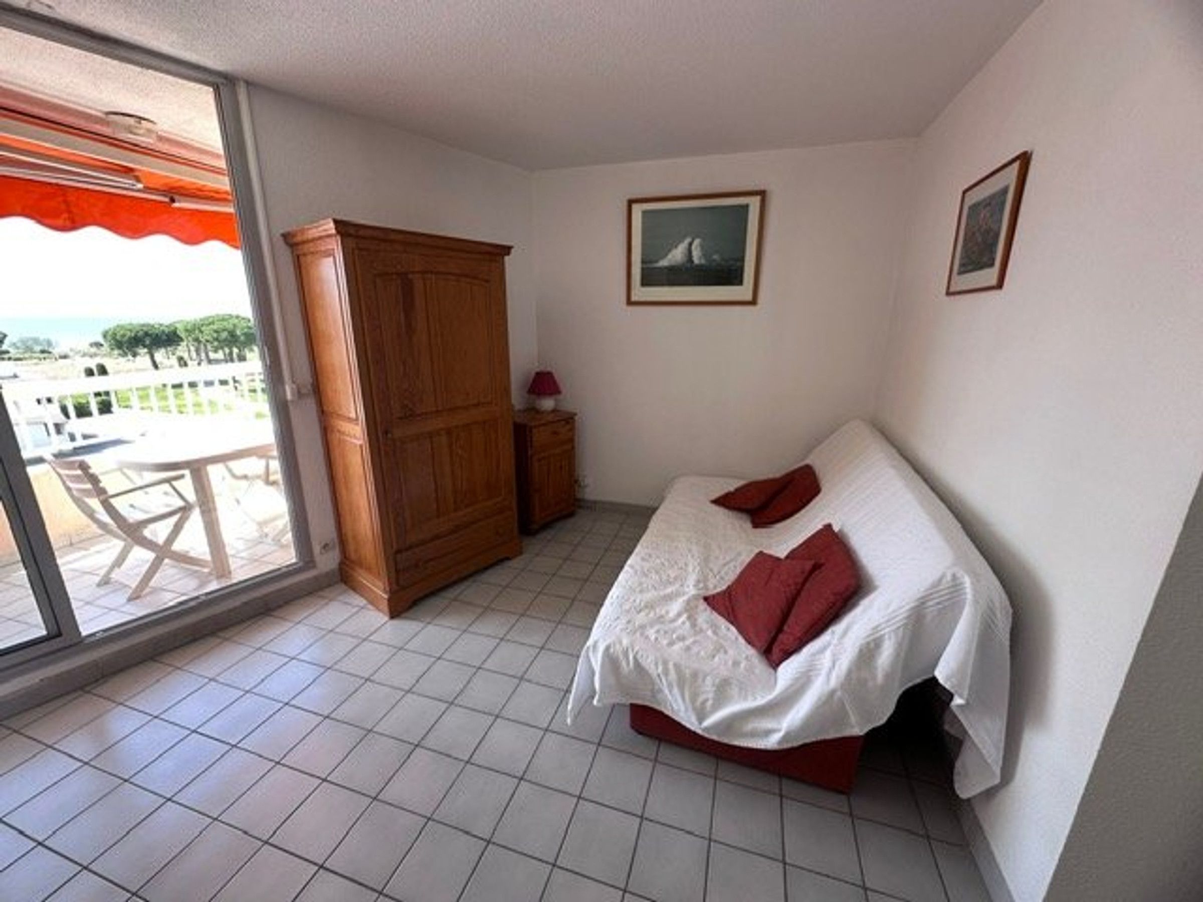 A bedroom with a bed, a wooden wardrobe, a small bedside table, and a window with a view of the outside.