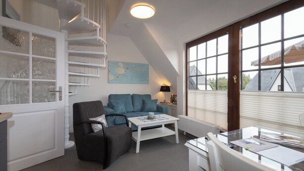 A modern living room with a staircase, a blue sofa, a coffee table, and a dining area with a table and chairs.