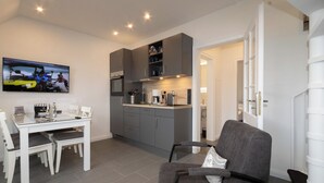A modern kitchen with grey cabinets, a dining table with chairs, and a TV mounted on the wall.