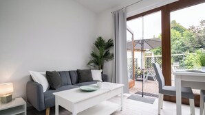 A modern living room with a grey sofa, white coffee table, and a view of the garden through large sliding doors. - Hochwertiges 1-zi-app für 2+1 Pers. am See, Wlan, Terrasse, Elektr. Kamin (Mirow)