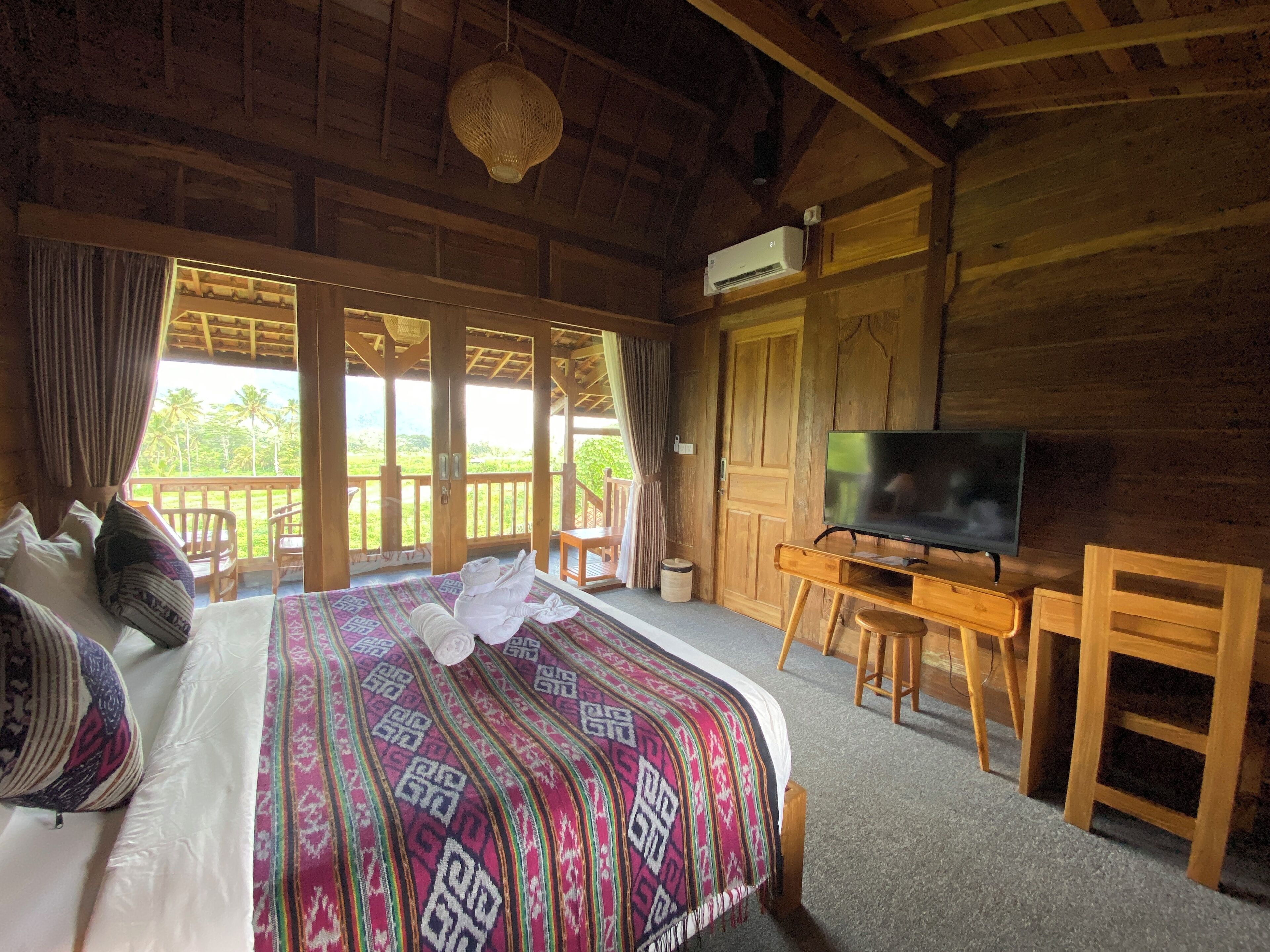 Habitación de cabaña de madera con cama, televisor y balcón con vistas a la vegetación.
