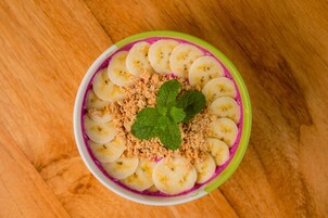 A bowl of food with bananas, granola, and a purple substance, possibly a fruit or yogurt, on a wooden surface.