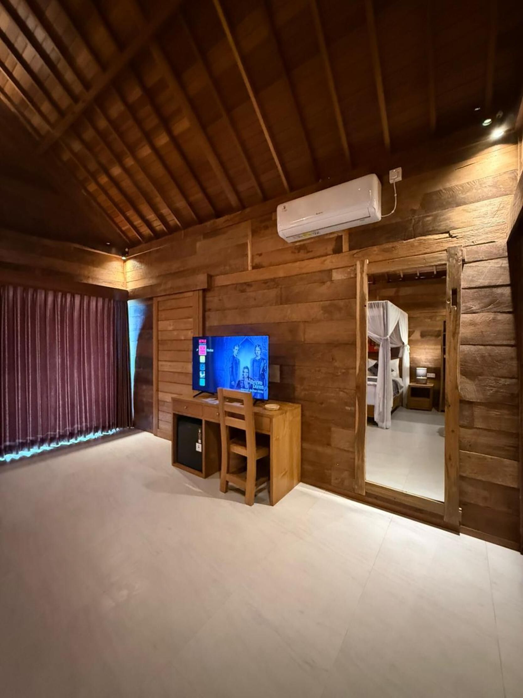 A wooden cabin interior with a television, a desk, and a bed with a canopy.