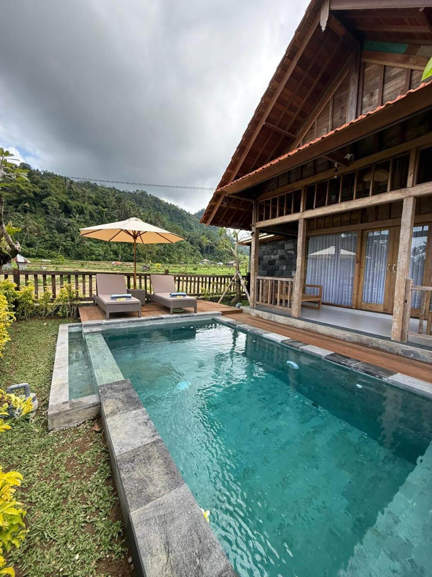 A swimming pool with a wooden deck, lounge chairs, and a view of a lush green landscape.