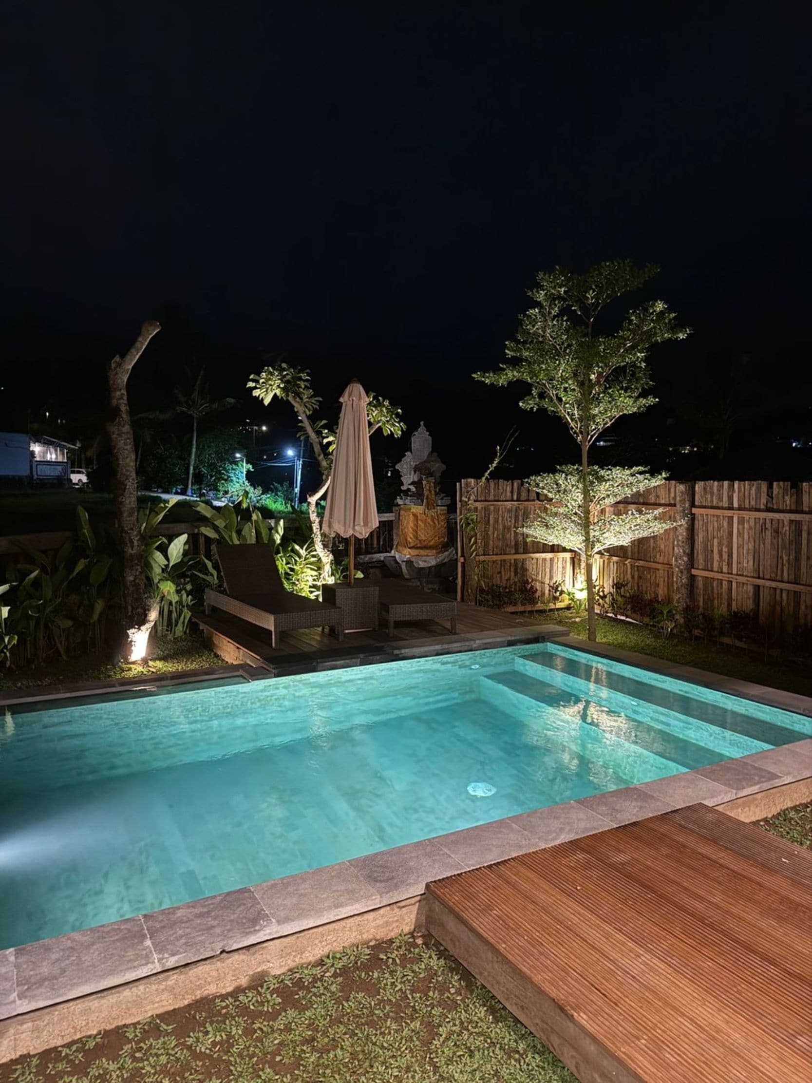 Une piscine avec une terrasse en bois, un espace salon couvert et une clôture en bois.