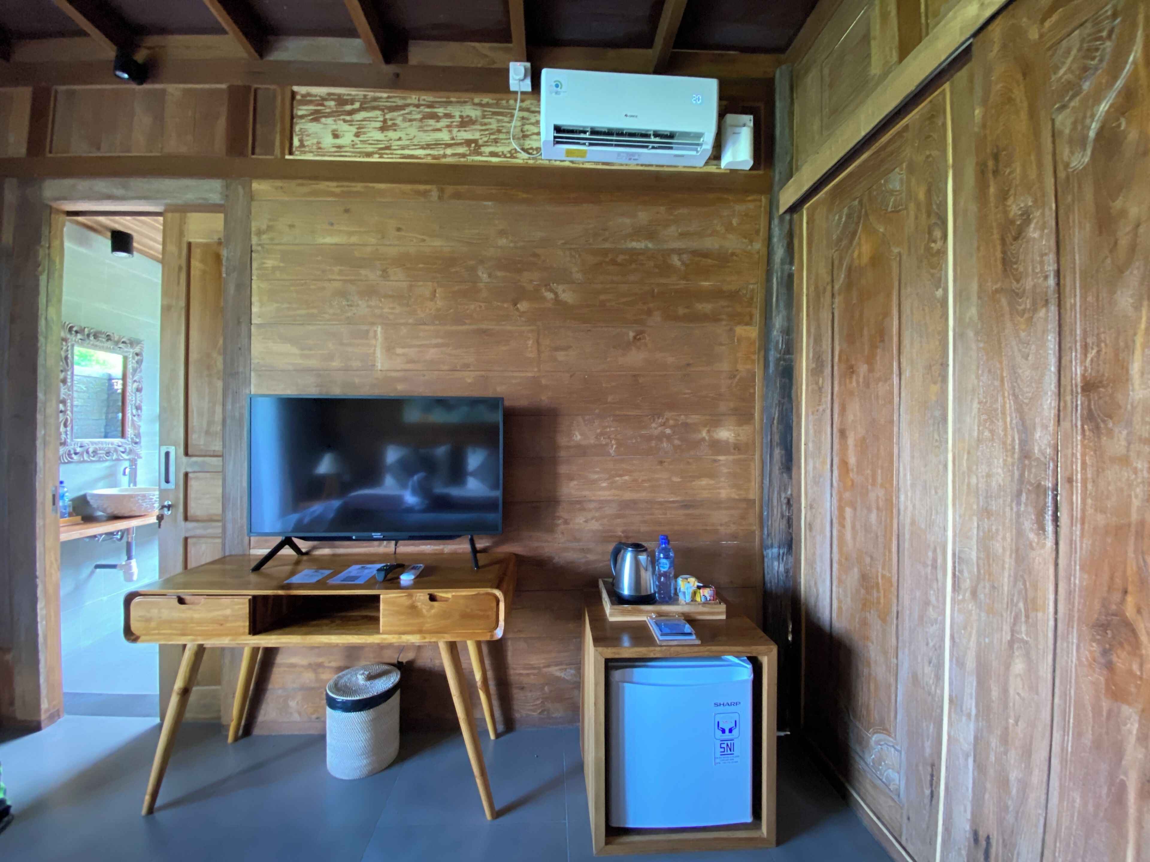 A wooden interior with a television on a wooden stand, a small refrigerator, and a trash bin.