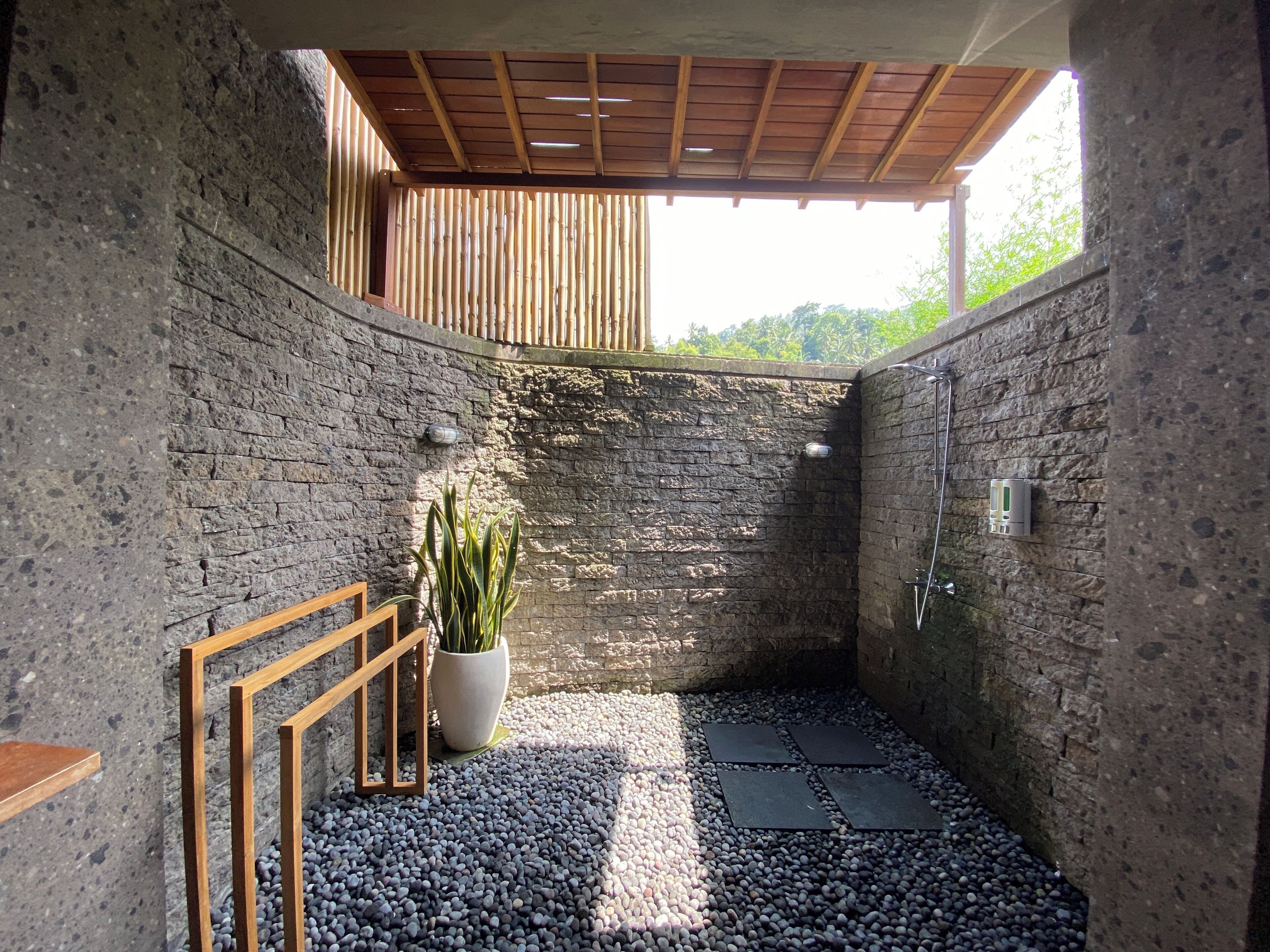 A modern bathroom with a stone wall, a wooden bench, a potted plant, and a shower area.