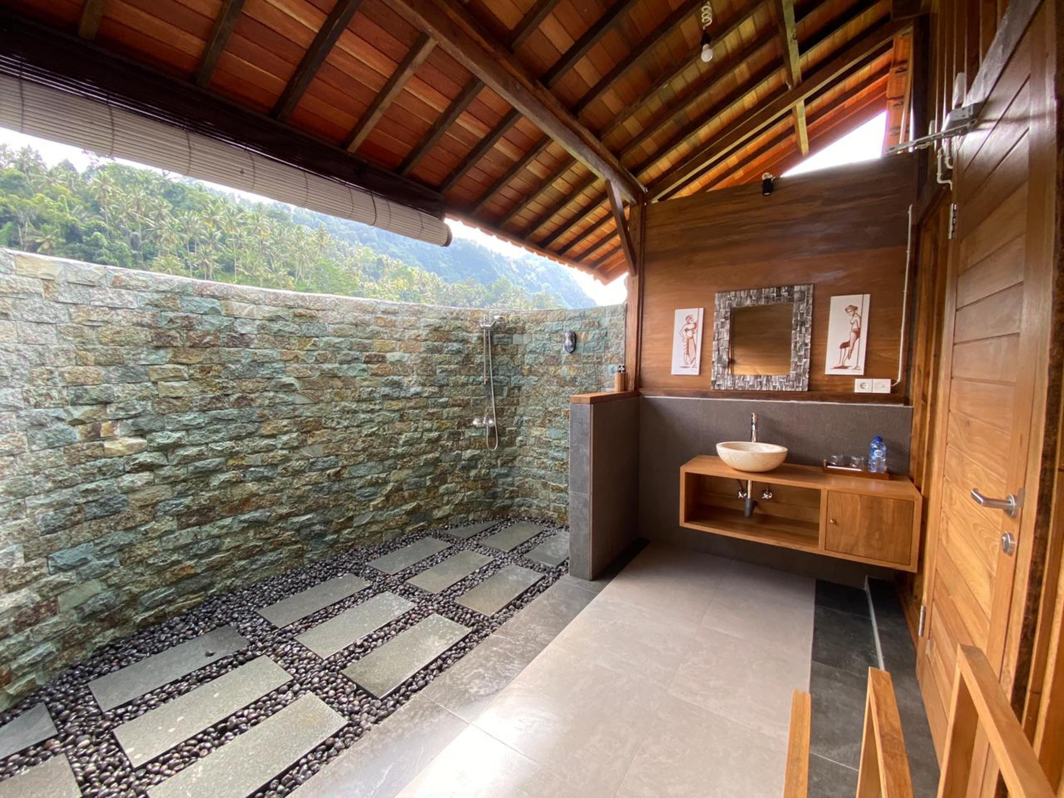 A bathroom with a stone wall, a wooden vanity, a large mirror, and a shower area.