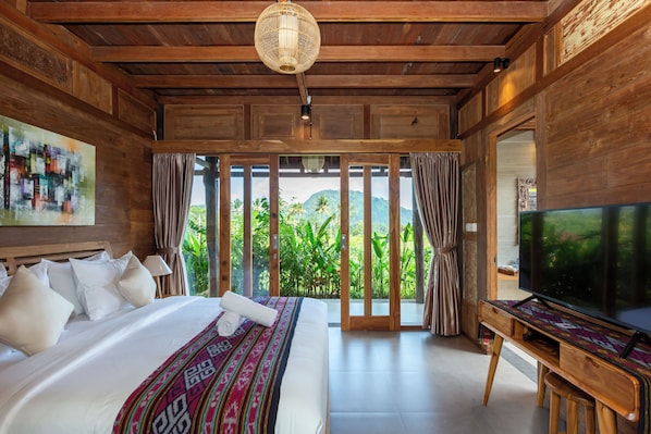 A spacious bedroom with a large bed, a television, and a view of lush greenery. - Kubu Sakian Villa  (Sidemen)