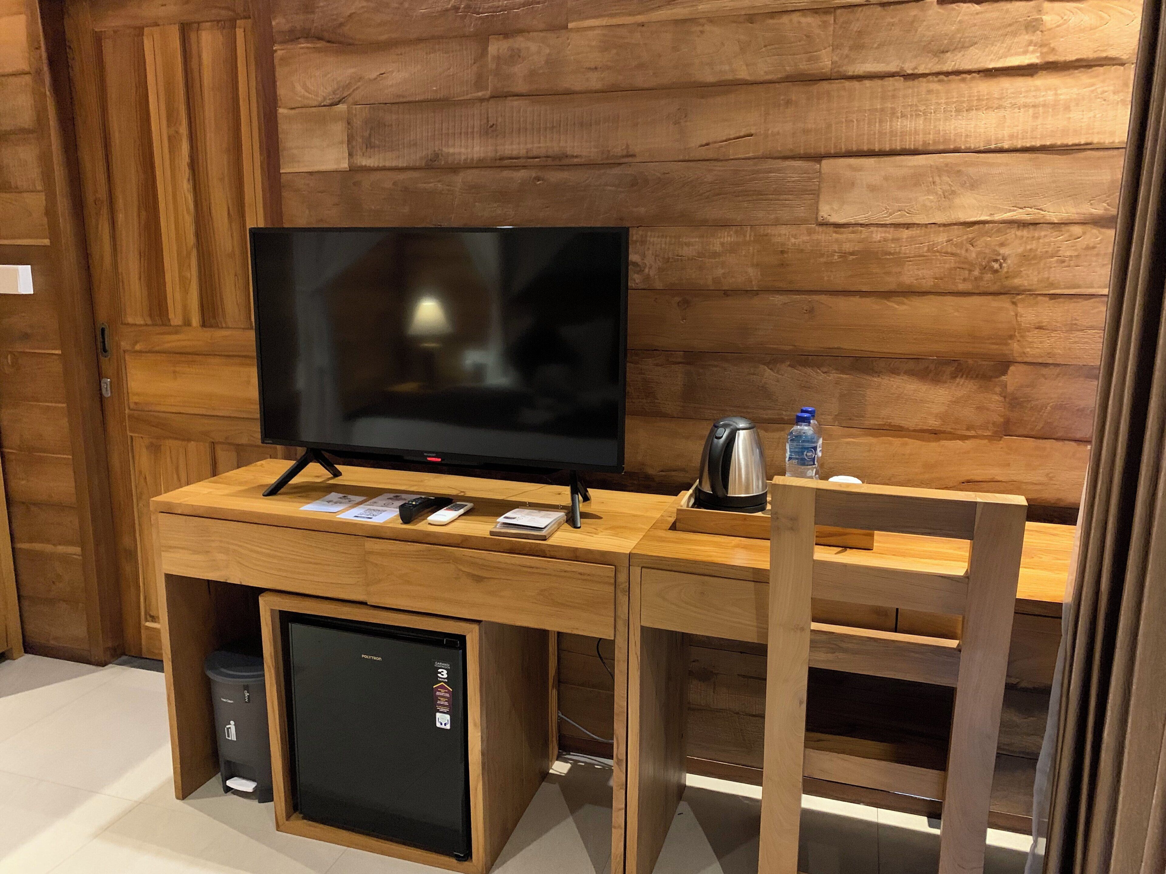 Un meuble en bois pour la télévision, avec un téléviseur à écran plat, une bouilloire et une bouteille d’eau.